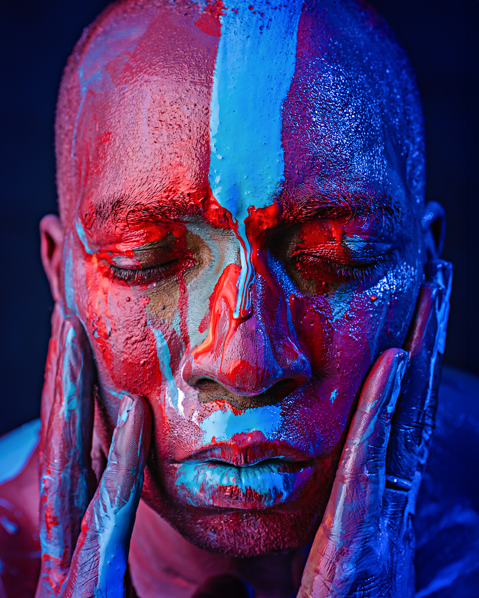 Conceptual artist branding portrait in Sammamish featuring a dramatic, close-up shot of a man's face covered in vibrant red and blue paint, captured during a professional studio session.